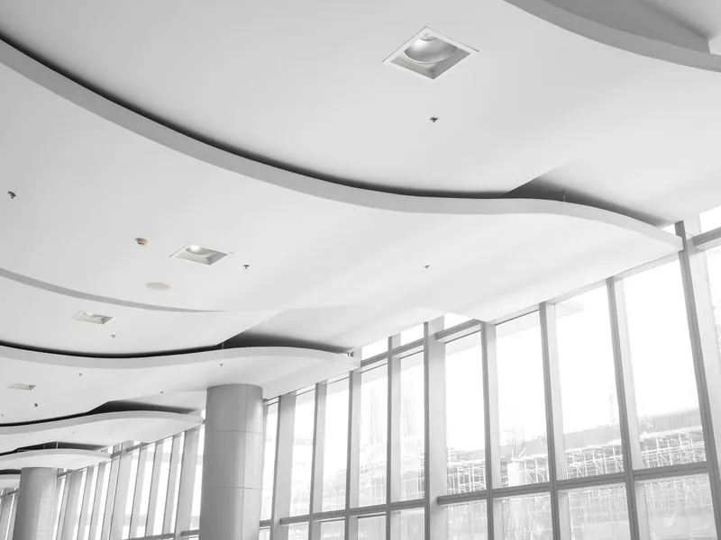Curved white gypsum ceiling with recessed lights beside a glass facade