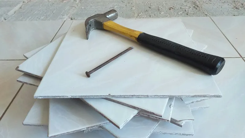 Hammer and nail resting on a stack of removed white floor tiles
