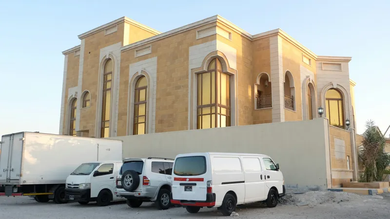 فيلا كبيرة مكسوة بالحجر بنوافذ مقوسة وسيارات متوقفة خارج السور